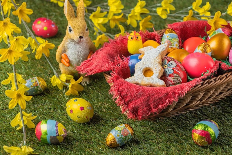 A basket full of colorful Easter eggs and a rabbit figurine with yellow flowers and chocolate eggs