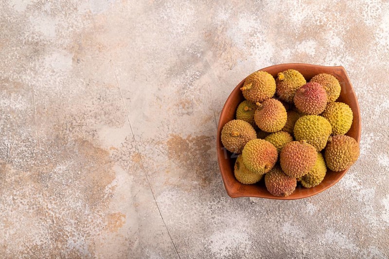 Ripe Lychee on clay bowl on brown concrete background, top view, flat lay, copy space, minimalism