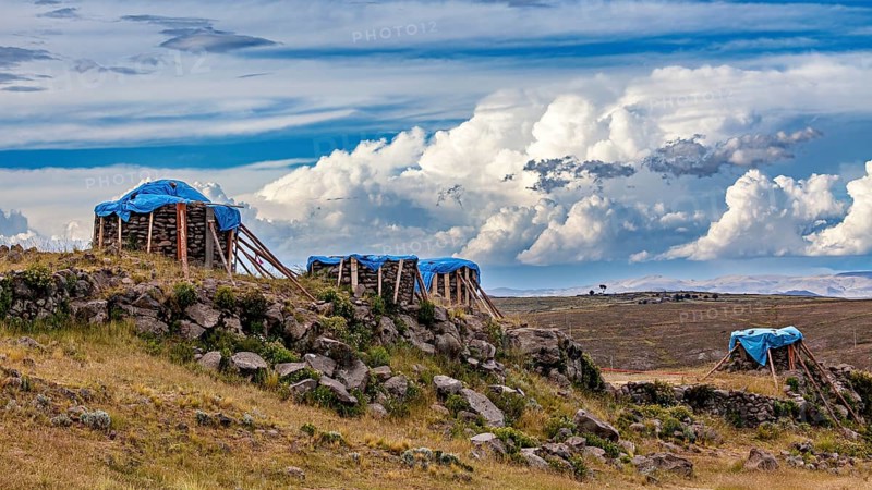 Structures covered with tarps, on a grassy hill under a cloudy sky, The Chullpas of Sillustani near Puno in Peru