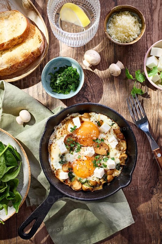 Fried eggs with spinach, mushrooms, grated cheese and feta cheese in small cast iron skillet. Top view