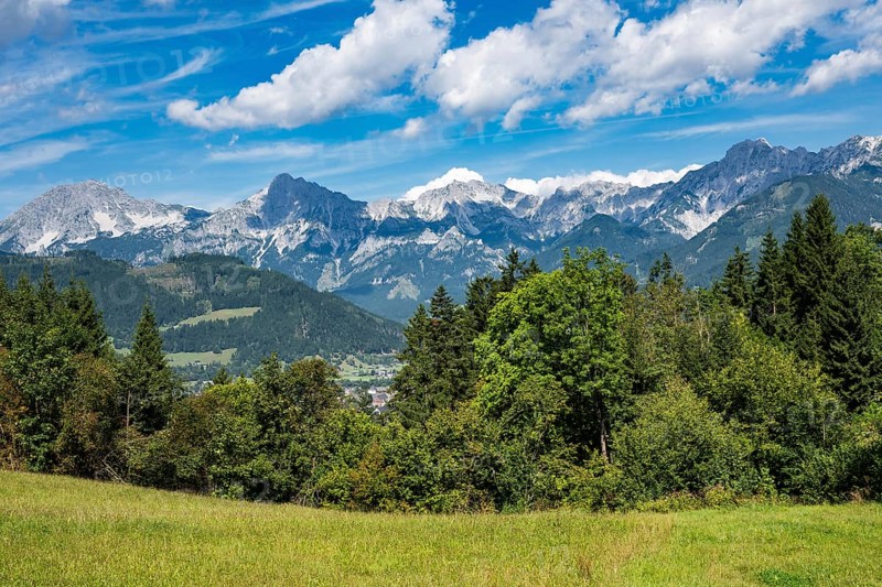 A picturesque landscape of the Austrian Alps nestled in lush green meadows beneath jagged, towering mountain peaks in Austria