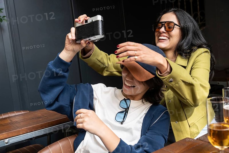 A joyful couple captures a happy moment together with a camera. They are laughing, expressing happiness and love. Glasses of drinks are visible on the table