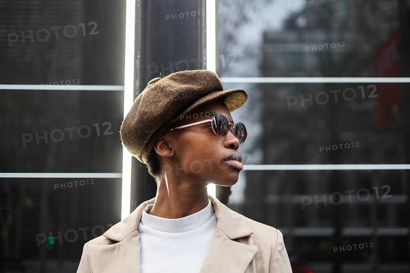 Stylish black woman in sunglasses and a brown hat, radiating urban elegance Captures modern, confident fashion with an ethnic flair against a city backdrop