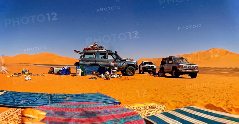 Off-roaders and camping equipment in the middle of a vast desert landscape under a blue sky, with off-road vehicles through the Sahara desert in Algeria
