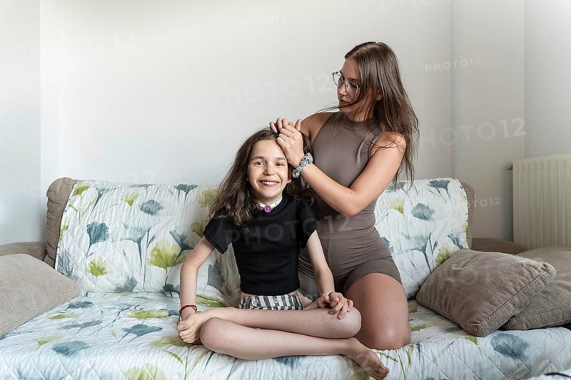 A loving family moment, highlighting a young girl with a tracheostomy being cared for by her sister. This heartfelt scene is set in a cozy home environment, emphasizing support, care, and joy