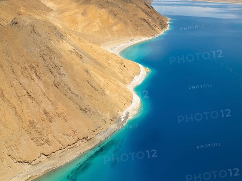 A breathtaking aerial view of Pangong Tso lake in Ladakh, India, showcasing its vibrant blue waters bordered by rugged, arid mountains of the Himalayan range