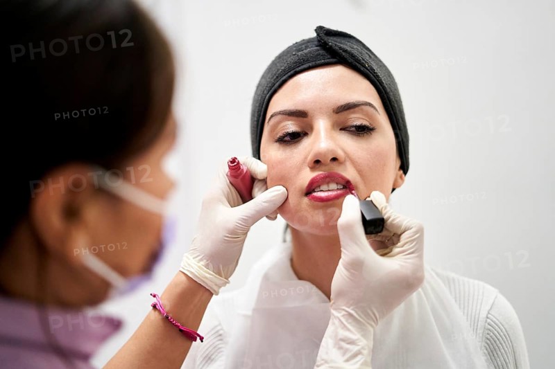An experienced technician applies makeup to a client's lips in a beauty salon focused on aesthetic medicine. This setting promotes relaxation and professional beauty services