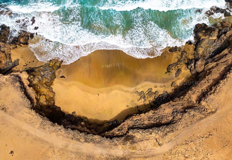 Top view aerial shot of a secluded natural pool at Tindaya Beach in Fuerteventura, Canary Islands, showing contrasting textures of rocky shores and golden sands surrounded by turquoise waters