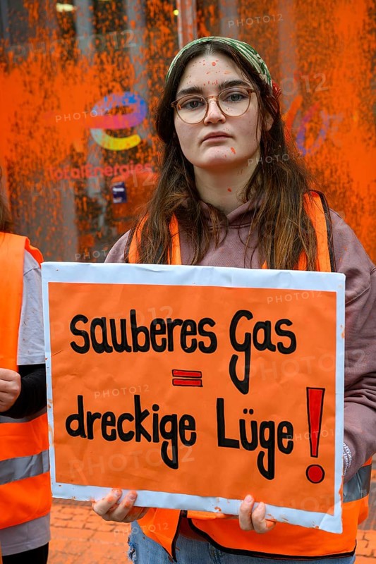 Lilli Gomez, Last Generation activist after colour attack on Total Energies building. They are protesting against the World LNG Summit, which is due to take place in Berlin in December. The poster reads: Clean gas = dirty lie!, Berlin, 06.11.2024