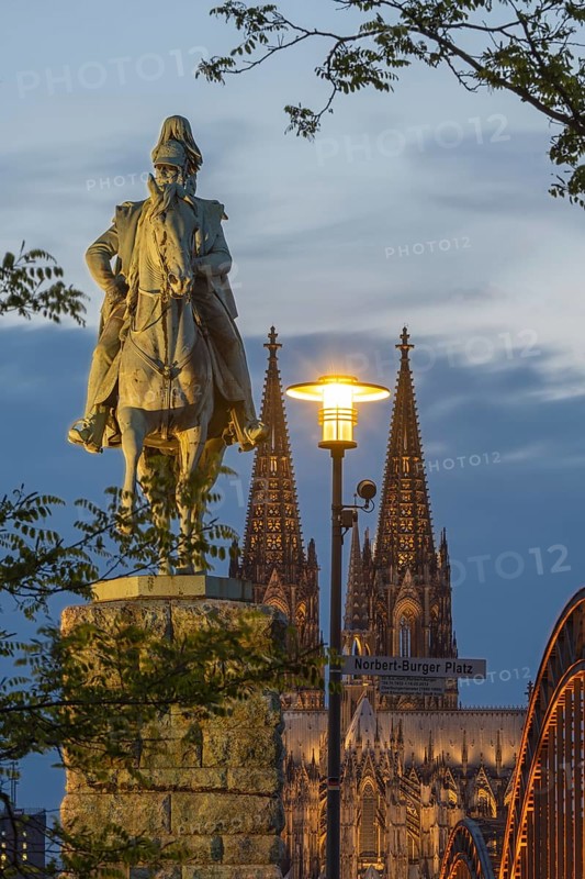 Equestrian statue of Kaiser Wilhelm I on Norbert-Burger Platz, with Cologne Cathedral and the Hohenzollern Bridge illuminated with LED lights behind it, Cologne, North Rhine-Westphalia, Germany
