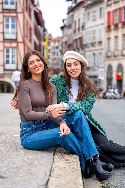 Vertical photo of a two young stylish friends sitting on a beauty square in the city