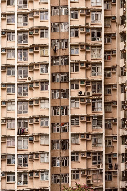 The image captures the facade of a high-rise residential building in Hong Kong. Numerous air conditioning units and hanging clothes reflect the dense urban lifestyle