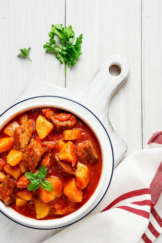 Potatoes stewed with meat, in tomato sauce, with spices and herbs, no people, on a white table