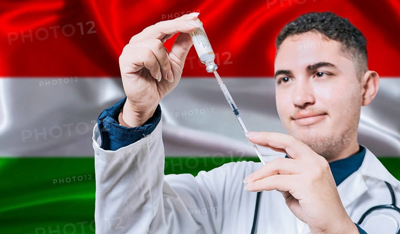 Doctor holding syringe on Hungary flag background. Medical professional holding syringe with Hungarian flag in the background
