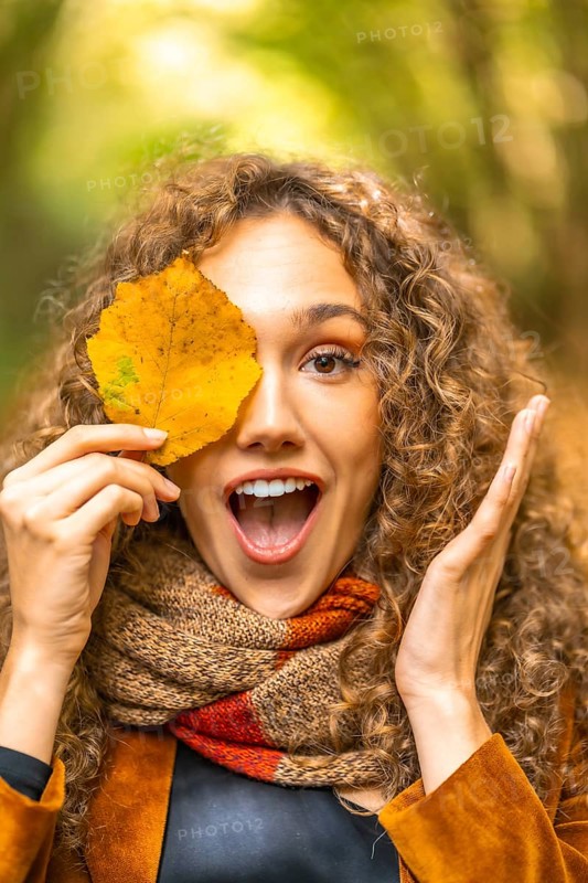 Vertical portrait of a playful woman hiding among yellow leaf