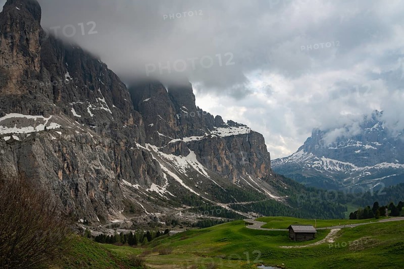 Majestic view of Val di Funes in the Dolomites, Italy, featuring rolling green hills, rugged cliffs, and a serene mountain landscape under a dramatic cloudy sky