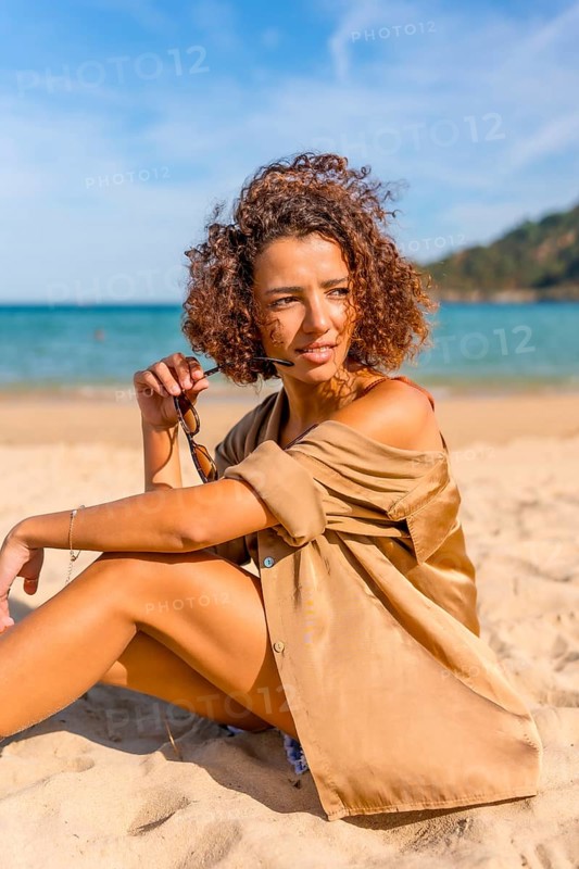 Vertical photo of a beauty arab young woman taking off the sunglasses enjoying day sitting at beach