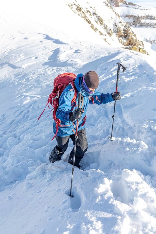 A skier in winter gear climbs a snow-covered mountain with poles and a backpack. The bright winter scene captures the spirit of adventure and the beauty of nature