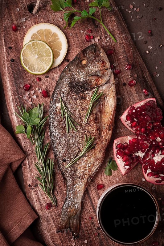 Fried dorado fish, with spices and herbs, on a wooden board, pomegranate sauce, close-up, no people