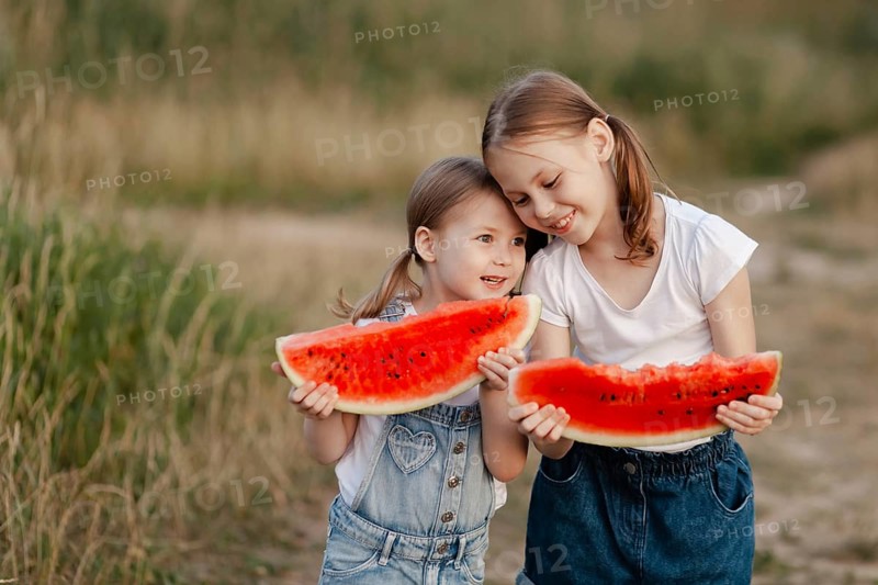Two joyful children savor large slices of watermelon outdoors during a bright summer day. Their happiness is enhanced as they enjoy this refreshing seasonal treat