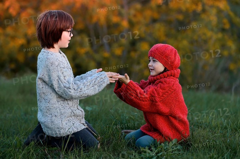 A girl and a boy, siblings, enjoy a playful moment outdoors on an autumn day, holding hands warmly in a park surrounded by colorful foliage