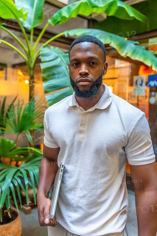 Vertical portrait of a casual and serious african man holding laptop outside a coworking office