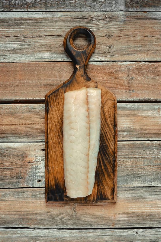 A clean, freshly sliced fillet of white fish rests on a handcrafted wooden cutting board