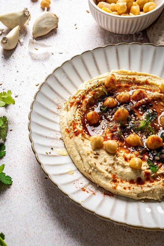 Creamy hummus served on a white plate, garnished with whole chickpeas, paprika, olive oil, and fresh herbs. Perfect for Mediterranean cuisine lovers