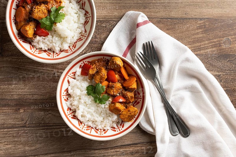Top view of two bowls of Hungarian pork goulash served with white rice, garnished with fresh parsley on a wooden table. A traditional dish styled in rustic tableware