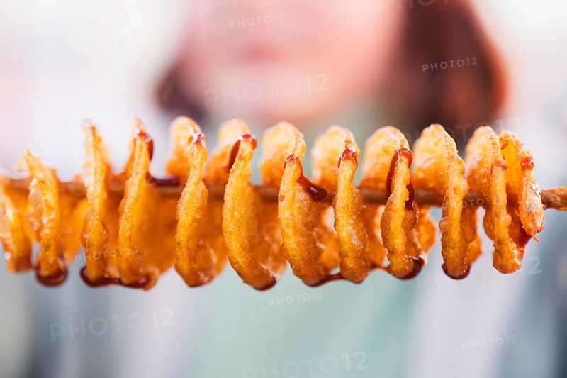 Close-up of golden spiral tornado potatoes on a stick, drizzled with sauce. This tasty snack is popular at fairs and festivals for its unique presentation and flavor