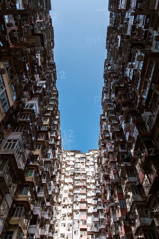 From below a dramatic view of dense residential buildings in Hong Kong. High-rise structures crammed together showcase the city's unique architecture and urban density under a bright sky