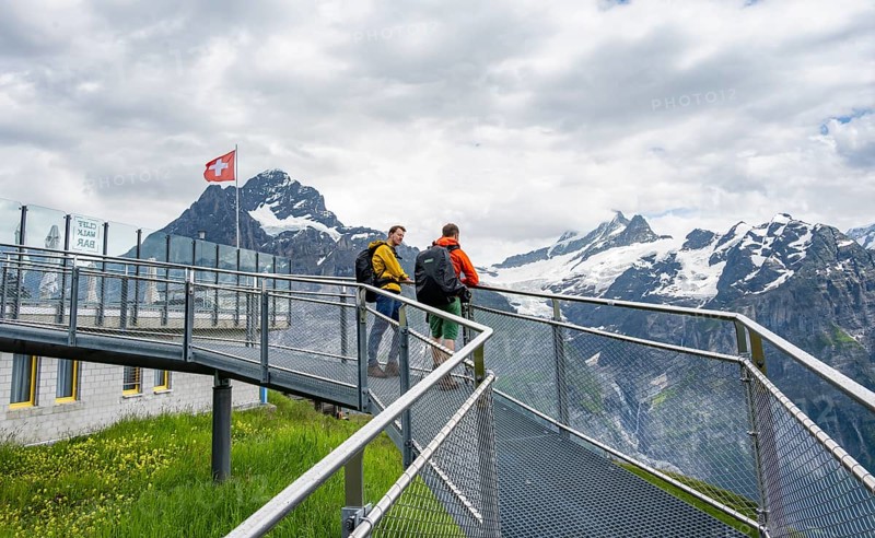 Tourists on the First Cliff Walk, metal trail on a rocky outcrop, Grindelwald First, in front of impressive mountain landscape with Schreckhorn summit and Upper Grindelwald glacier, Bernese Alps, Bernese Oberland, Switzerland