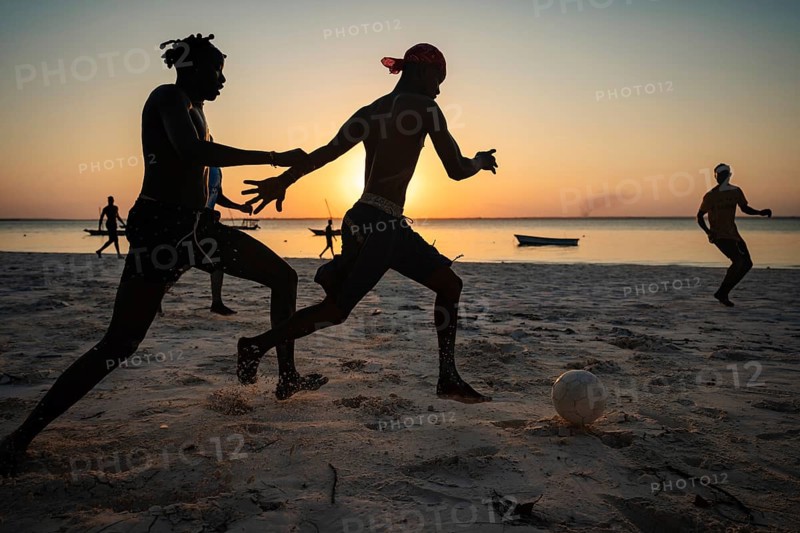 MICHAMVI KAE, ZANZIBAR - OCTOBER 19, 2025: Silhouetted young men play a competitive game of soccer on a white sand beach during sunset in Zanzibar