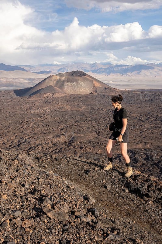 Woman on a hike through rocky terrain with volcano in the background, Argentina, volcanoes, lava field, Antofagasta
