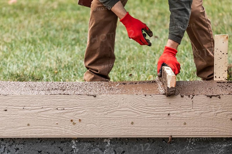 Construction Worker Leveling Wet Cement Into Wood Framing