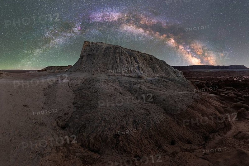 A stunning panoramic view of the Milky Way galaxy arched above a unique rock formation in Goblin Valley State Park, Utah, showcasing the breathtaking night sky against the desolate desert landscape