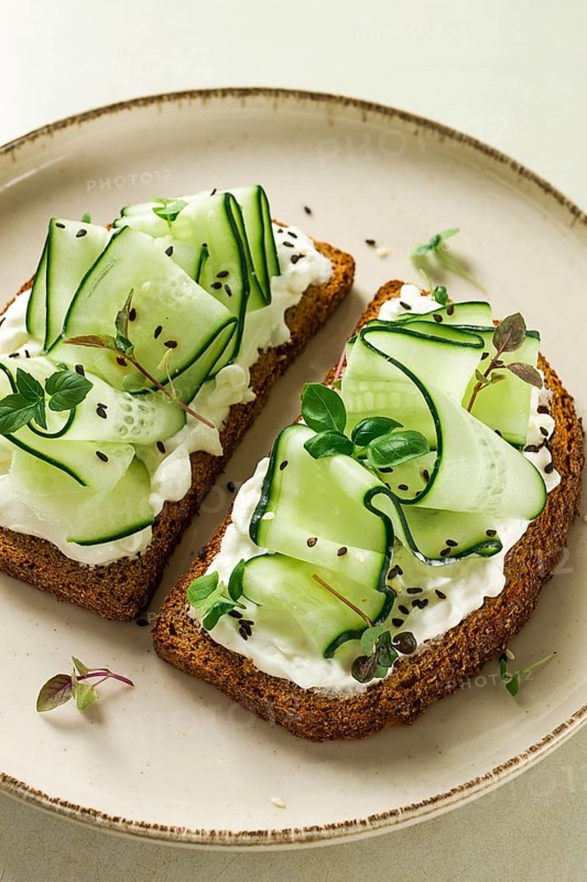 Breakfast, cereal bread sandwiches, cream cheese, sliced cucumber, with micro greenery on a light table, close-up, top view, selective focus, no people