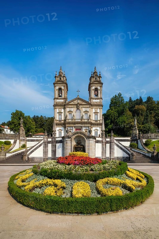 Centered composition of the Bom Jesus do Monte church and sanctuary in Braga, Portugal, with a formal floral parterre, fountain niche and symmetrical stairs under a luminous sky