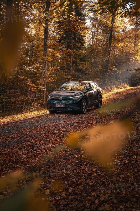 Car on a leafy path in autumn forest, flooded with sunlight, electric car VW ID5, Gechingen, Black Forest, Germany