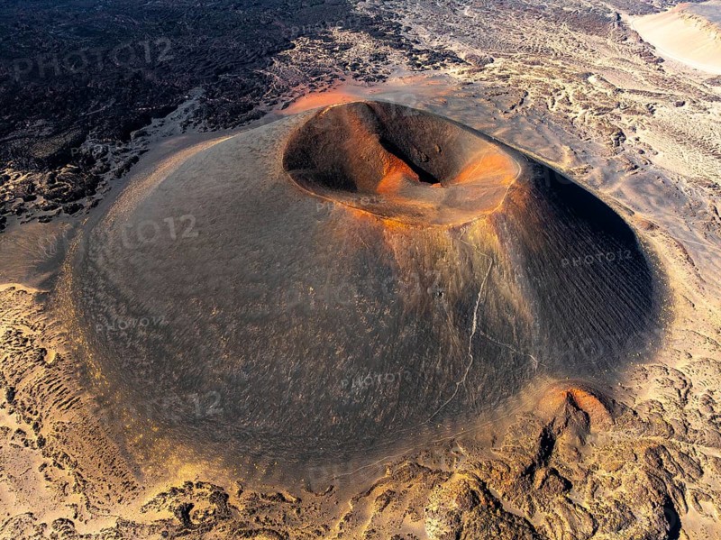 Aerial view of the majestic Antofagasta Volcano in Catamarca, Argentina. The sunrise casts a vibrant glow over its distinctive crater and rugged terrain, creating a stunning scene