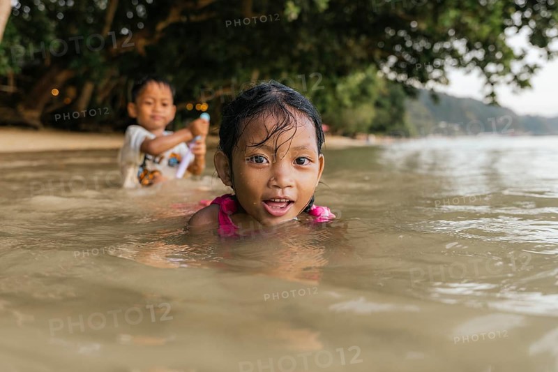 Two children enjoy playing in the ocean water on a beach in the Philippines. A girl in the foreground is smiling, with a boy in the background holding a toy
