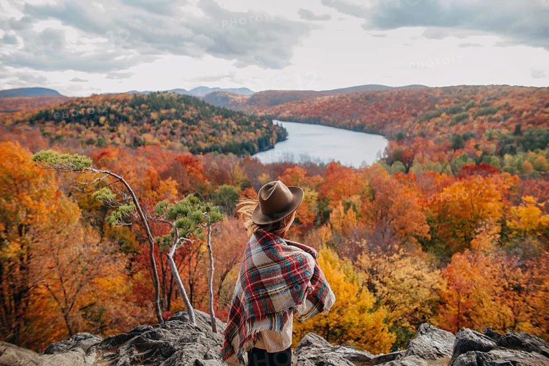 A lone traveler enjoys the breathtaking view of Quebec's autumn foliage. The vibrant colors of the forest reflect in the serene lake, creating a picturesque scene