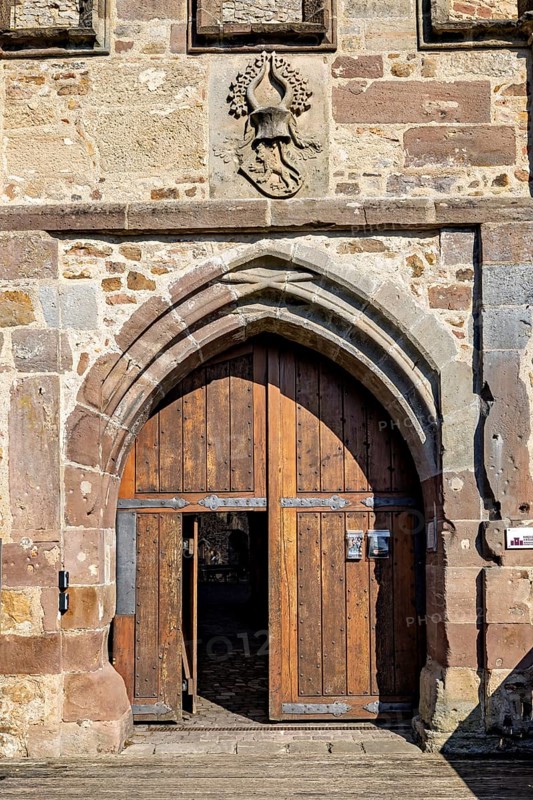 Large wooden gate in a robust stone wall with a heraldic coat of arms, The gate of Spangenberg Castle