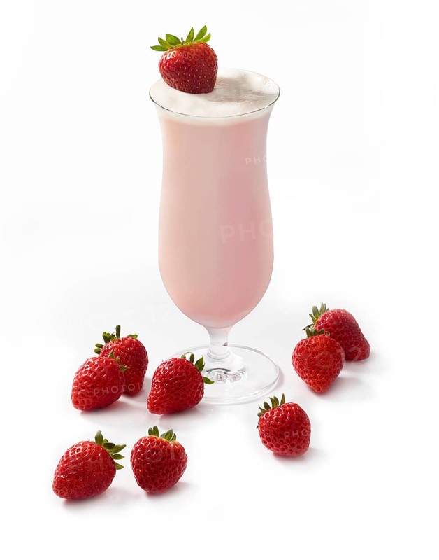 Cocktail in a long drink glass in front of a white background, a strawberry as garnish, strawberries as floor decoration, studio shot