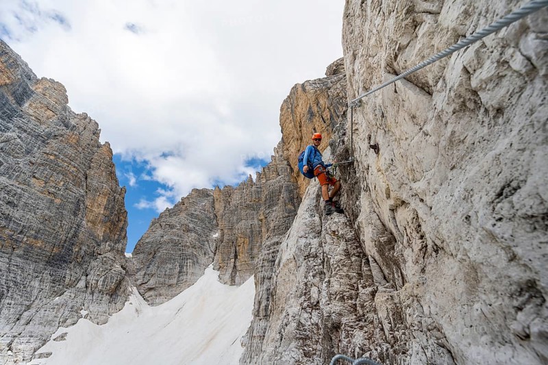 Mountaineer climbs on a steep rock face in the Via Ferrata Brentari via ferrata, spectacular mountain landscape with steep rock faces, remains of the Vedretta d'Ambiez glacier in the back, Brenta Mountains, Brenta-Adamello Nature Park, Trentino, Italy