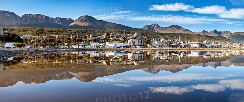 Panoramic shot of a city and mountain landscape with a dramatic reflection in the calm water, The city of Ushuaia in Argentina is reflected in the sea