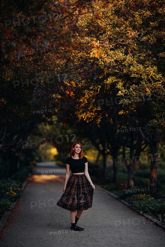A woman strolls through a Quebec park in autumn, surrounded by vibrant foliage. The path is lined with trees whose leaves display brilliant fall colors, creating a serene atmosphere