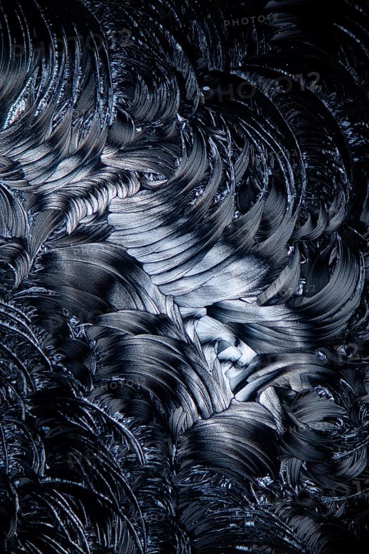 This close-up image showcases the fascinating, detailed swirled patterns of salicylic acid microcrystals magnified under a microscope, presented in black and white
