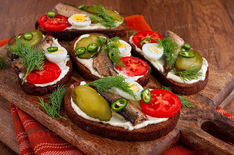 Sandwiches on rye bread with sprats, quail eggs, fresh tomatoes and pickled cucumber, on a wooden board, appetizer, breakfast