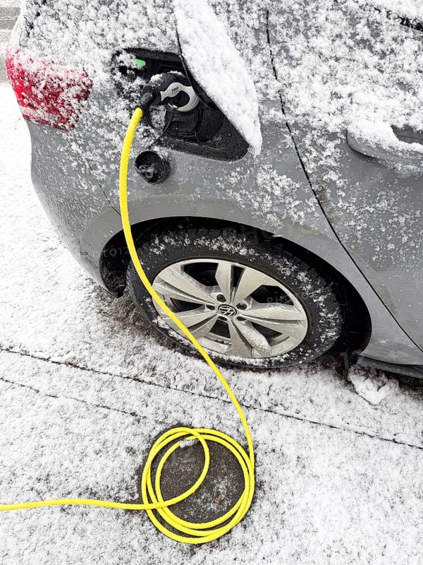 Charging an electric vehicle in winter. A yellow charging cable is connected to the car's charging socket while snow has accumulated on the bodywork, Düsseldorf, Germany